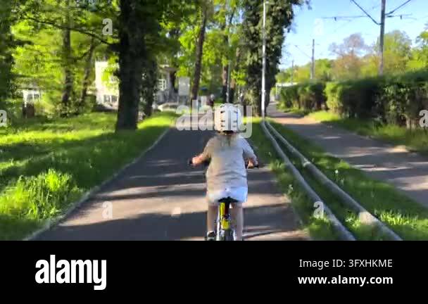 Young child pedals bicycle on quiet green cycling lane beneath tall ...