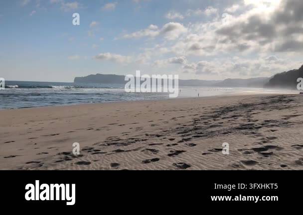 A vast sandy beach filled with footprints in the foreground, with ...