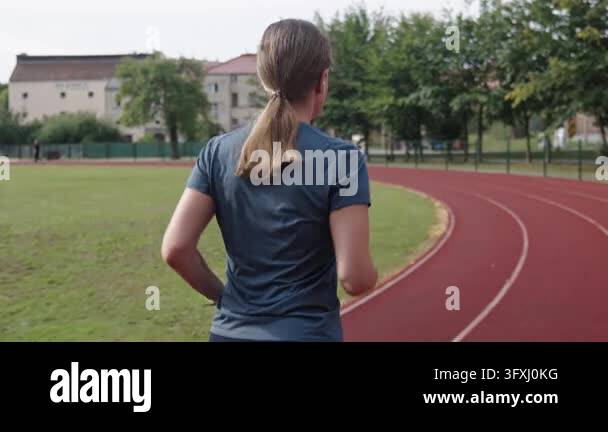 Woman running on stadium track during morning workout Back view of ...