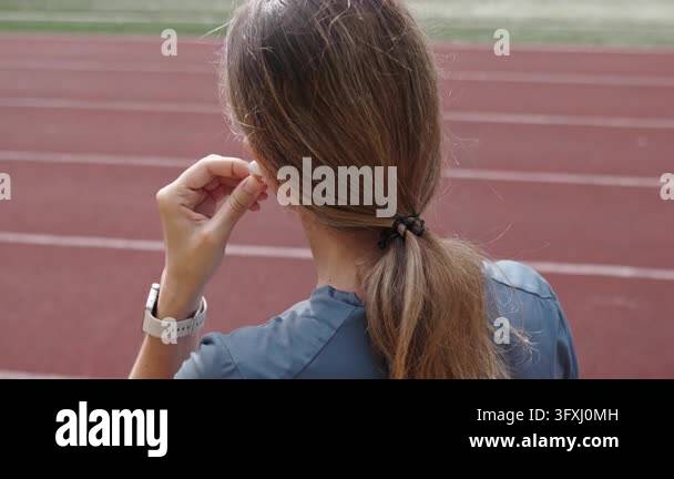 Woman putting in wireless earbud before running workout Back view of ...