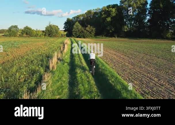 Cyclist riding along a grassy path between fields in the countryside ...