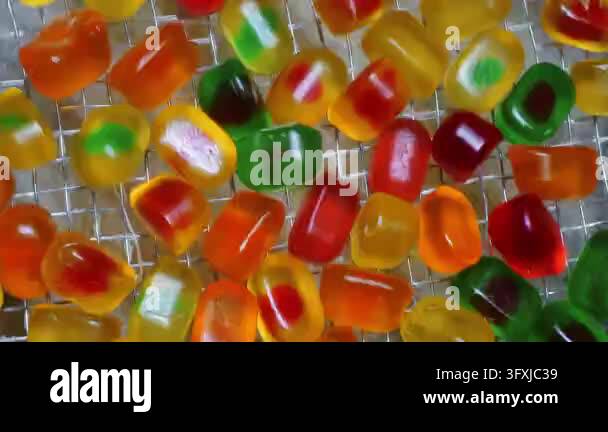 Close-up of colorful gummy candies moving along a mesh conveyor belt at ...
