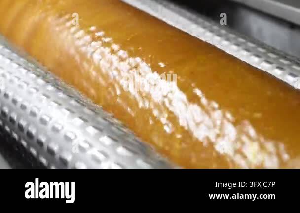 Close-up of glossy golden caramel mass moving through industrial ...