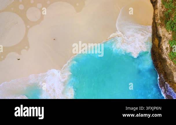 A lone woman walks along the white sand as turquoise waves crash ...