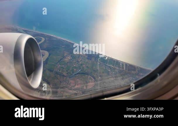 Aerial view from an airplane window showing a jet engine, winding river ...