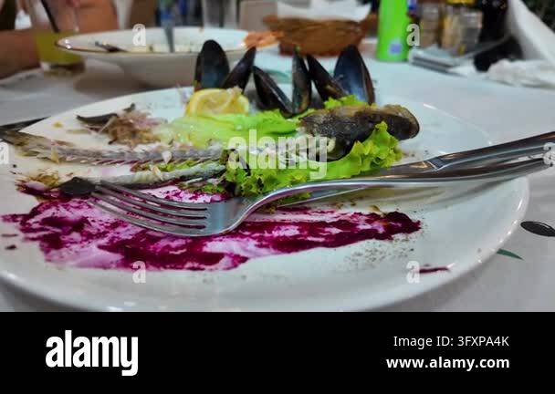 Dirty plate with remains of cooked fish, mussels, lettuce and sauce ...