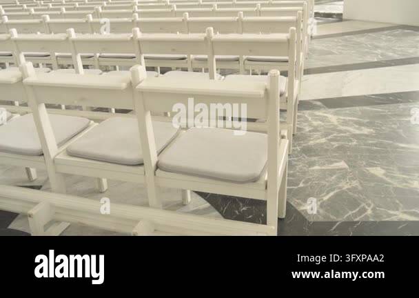 Repeating rows of white wooden pews fill the spacious interior of a ...