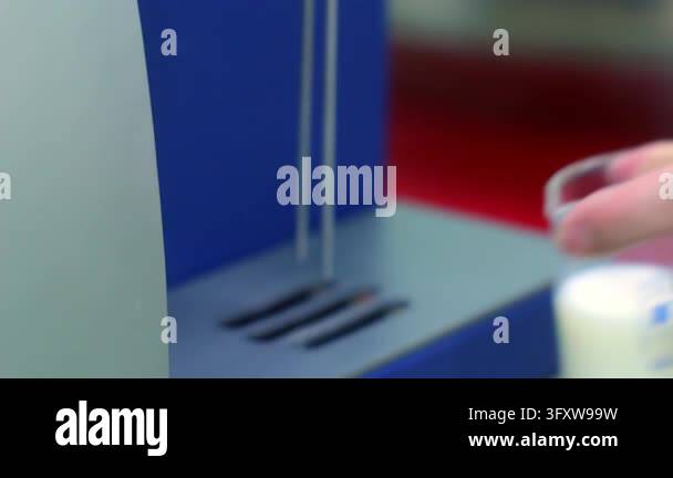 Hand placing glass beaker milk sample under analyzer probes, laboratory ...