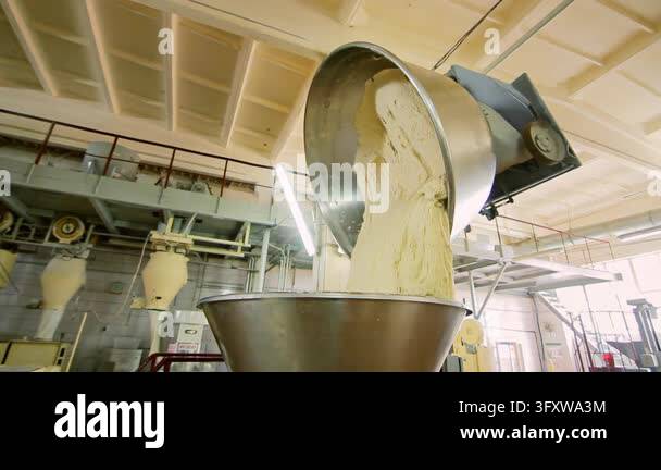 Kneaded dough unloading tilted steel mixer bowl into hopper, industrial ...