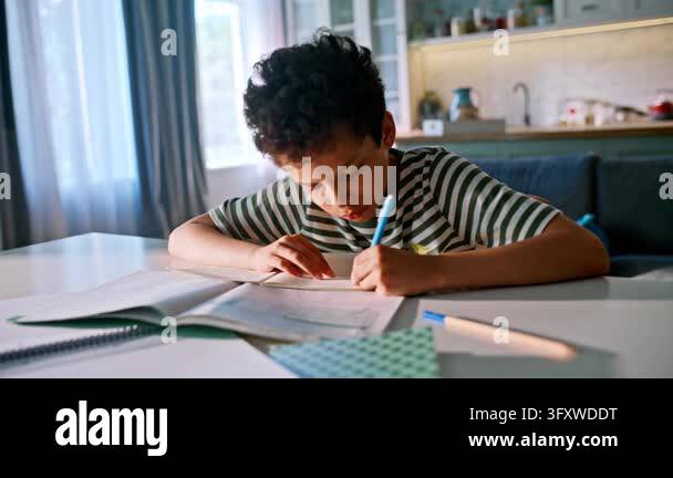 Schoolboy doing homework home kitchen table, writing pen exercise book ...