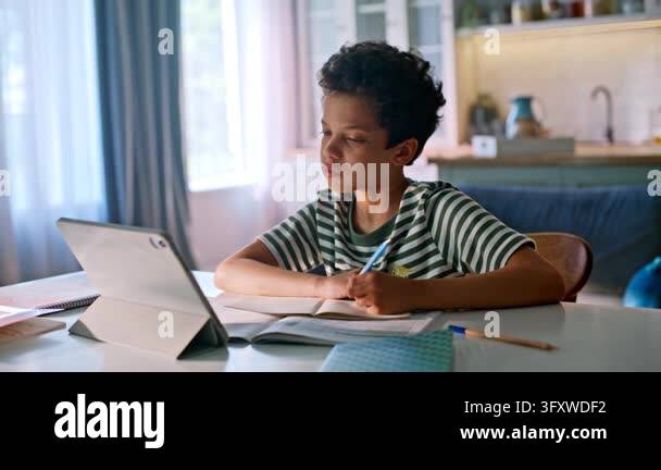 Schoolboy studying home kitchen table with tablet notebook. Mixed race ...