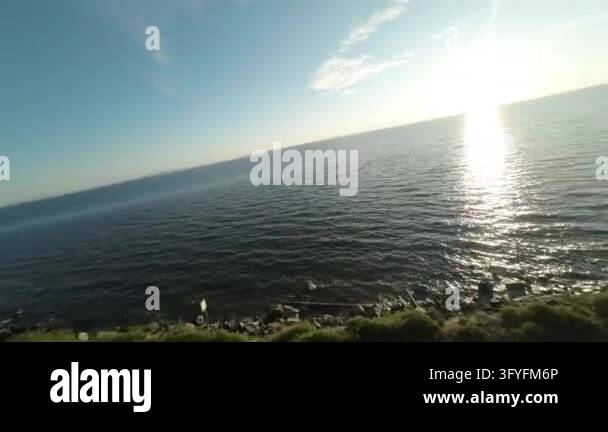 Eith Tracks Drone footage flying over a calm sea next to a rocky shore with trees ...