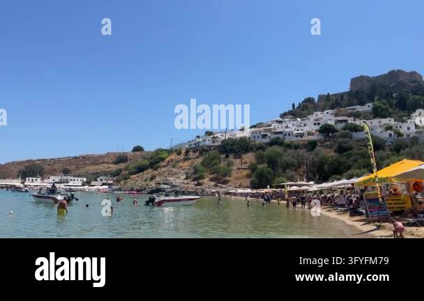 Acropolis of Lindos, People enjoying sunny day at crowded beach with ...