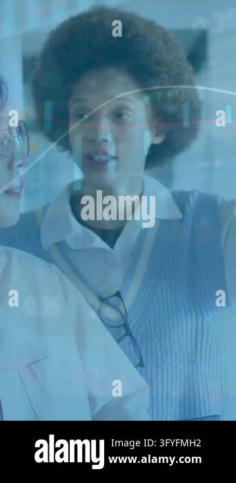 Analyzing data on glass board, two businesswomen with financial charts ...