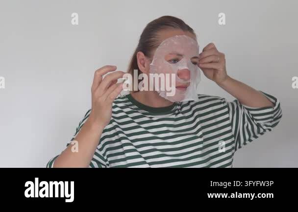Woman carefully adjusting a hydrating sheet mask on her face at home as ...