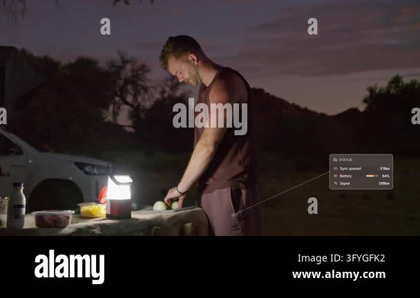 Man chops food at a camp table by lantern light in Namibia at dusk ...