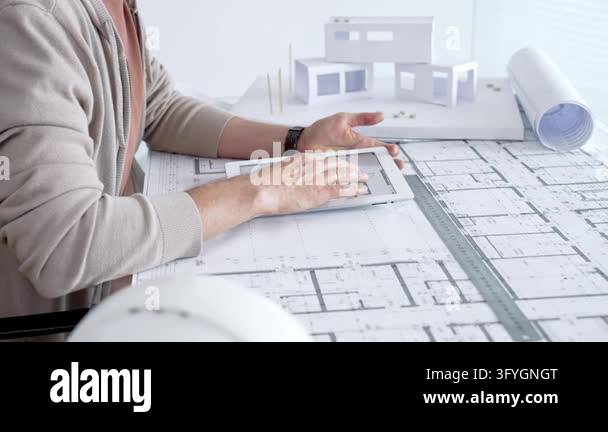 Architect reviews building plans on a digital tablet amid paper ...