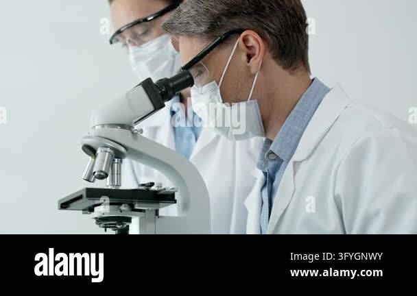 Scientist in safety gear looking into a microscope, conducting ...