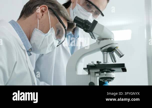 Scientist in safety gear looking into a microscope, conducting ...