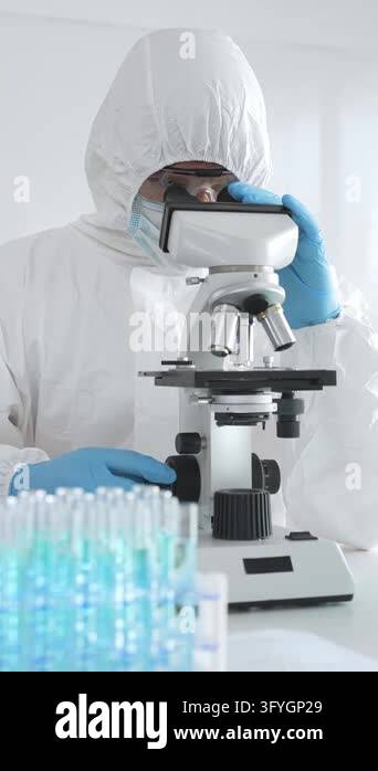Medical scientist wearing protective suit using microscope while ...