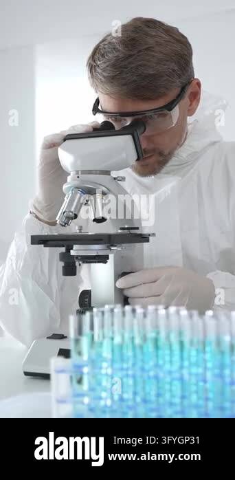 Medical scientist in lab coat and glasses using microscope while ...