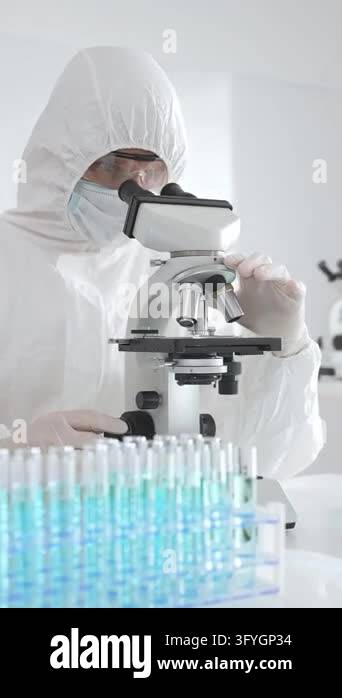 Medical scientist wearing protective suit using microscope while ...