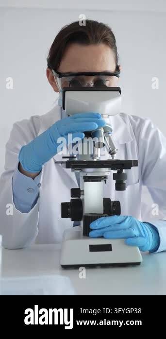 Female scientist wearing protective glasses and mask using microscope ...