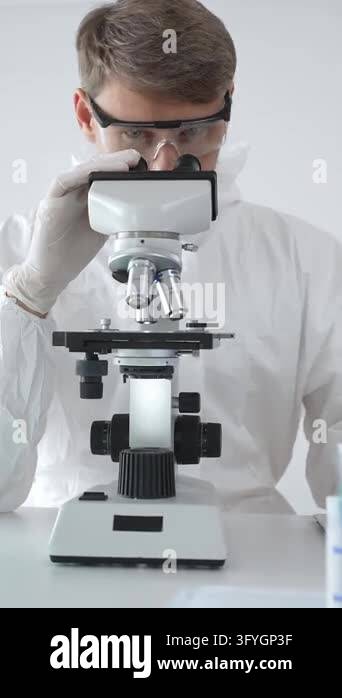 Medical scientist in lab coat and glasses using microscope while ...
