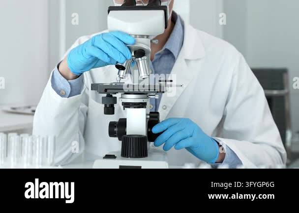 Scientist wearing safety glasses and blue gloves looking through bright ...