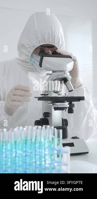 Medical scientist wearing protective suit using microscope while ...
