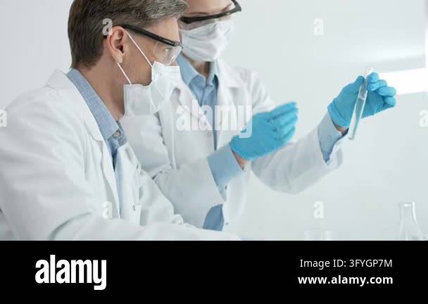 Analyzing liquid samples in test tubes, two scientists in safety masks ...