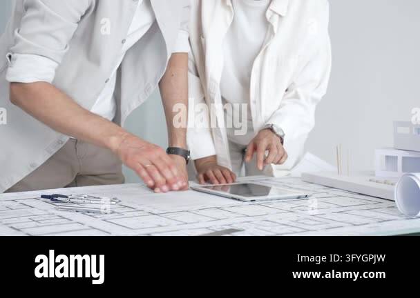 Two architects collaborate over blueprints and a scale model, measuring ...