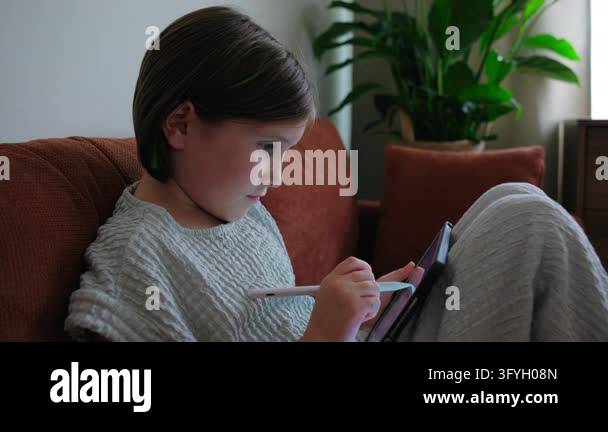 Side view of a focused girl sitting on an orange sofa in a cozy living ...