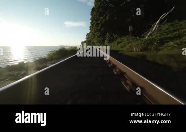 Tracking shot along railroad tracks beside the ocean with sun flare and ...
