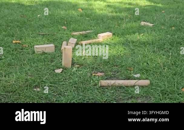 A baton bounces through a group of fallen kubb blocks on a green park ...