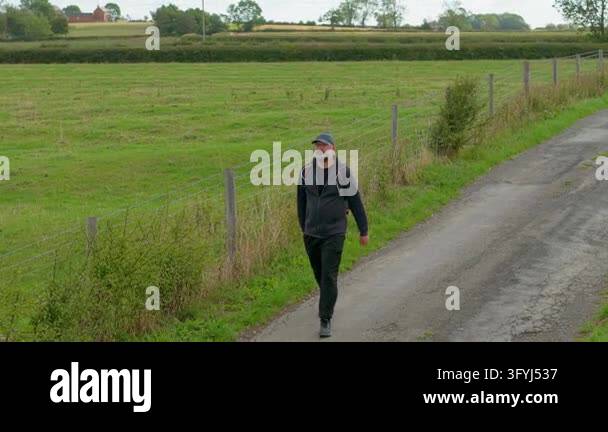 Rural hiker walking beside wire fence and green pasture on quiet ...