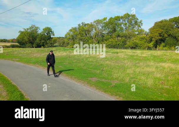 Man walking along rural country road beside green fields. Male hiker ...
