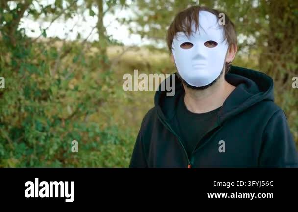 Maniac in white face mask walking through woodland in dark hoodie ...