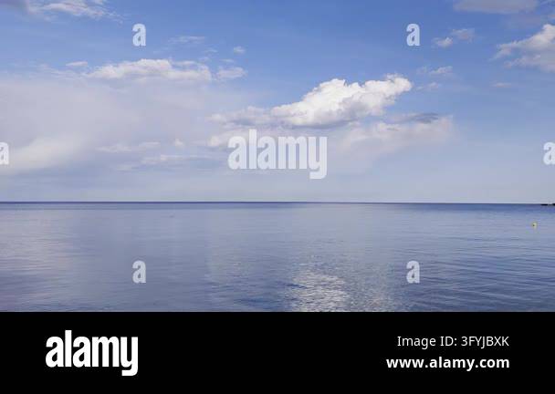 Calm blue sea reflects white clouds and sunlight under bright sky with ...