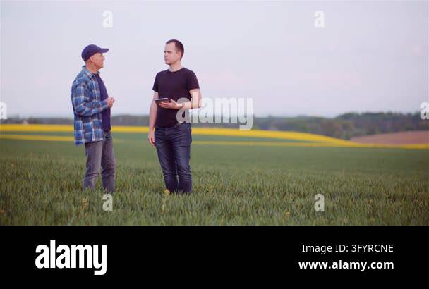 Two adult men stand in tall grass at the edge of an open countryside ...