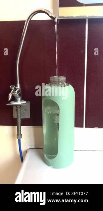 A thin stream of water pours from a metal faucet into a mint green ...