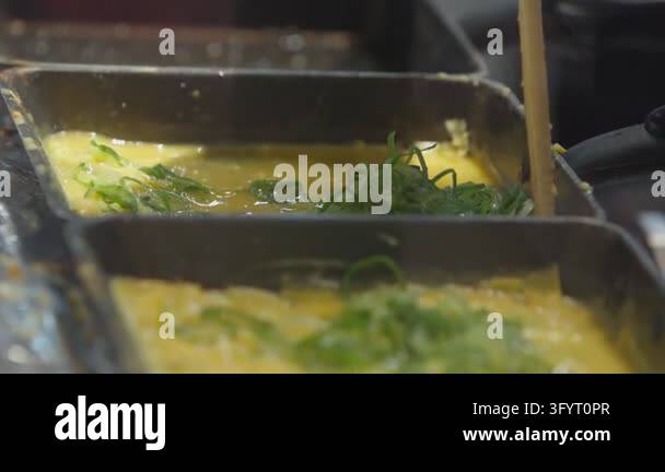 Scarllion In slow motion, chopsticks stir yellow beaten eggs and green scallion ...