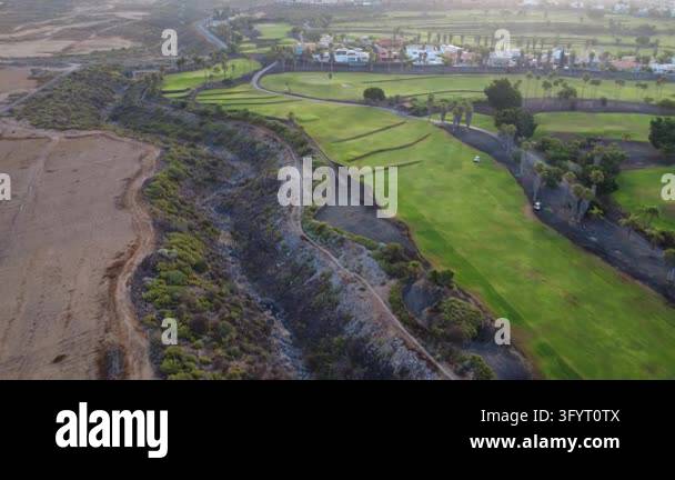 Aerial drone view of terraced green fairways beside a dry volcanic ...