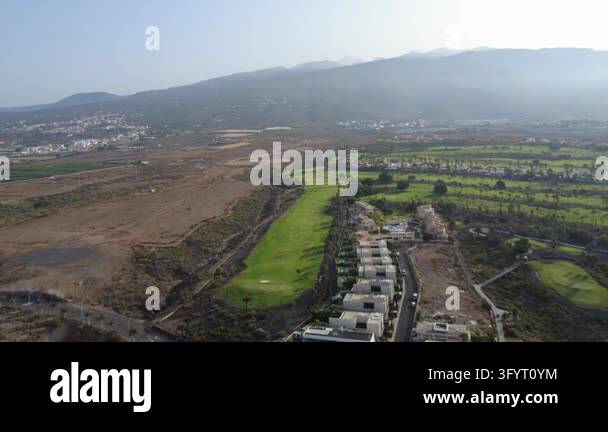 Aerial drone view of a green golf course and villas in a dry volcanic ...