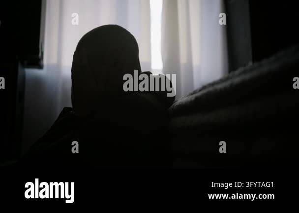 Depressed man sits in silhouette covering his face beside a bright ...