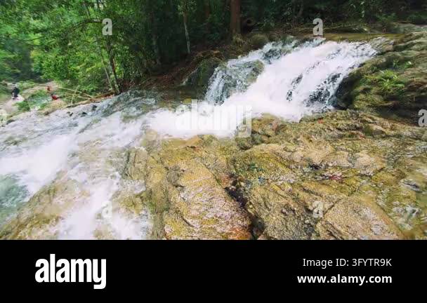 Visitors carefully explore a broad rocky cascade in a lush tropical ...