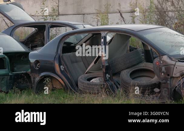 Dismantled car body shells sit abandoned outdoors near a concrete wall ...