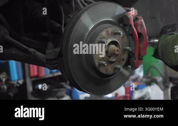 Auto mechanic cleans rust off a car brake caliper bracket with a rotary ...