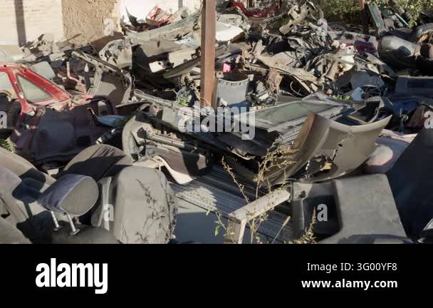 Dismantled automotive body panels and seats accumulate in an outdoor ...