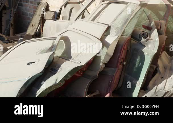 Dusty car doors stand stacked against a brick wall at an auto salvage ...